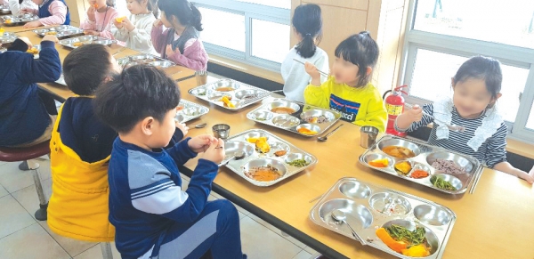 A초등학교 급식실에서 1학년 학생들이 성인용 수저와 젓가락을 사용해 점심을 먹고 있다.